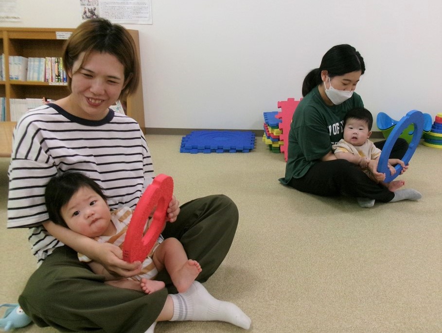 母の膝の上で車の運転を真似する赤ちゃんの様子