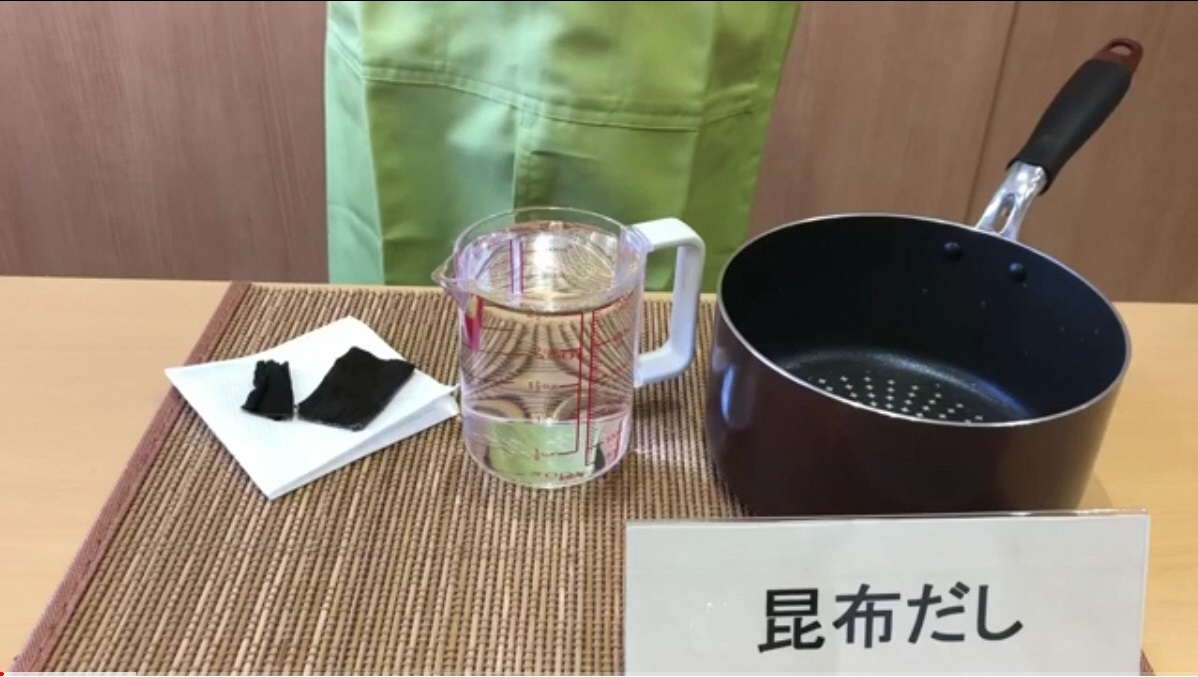 昆布だしと書かれた立て札のそばに昆布、水がたっぷり入ったビーカー、深底の鍋が並んでいる写真（YouTubeへリンク）