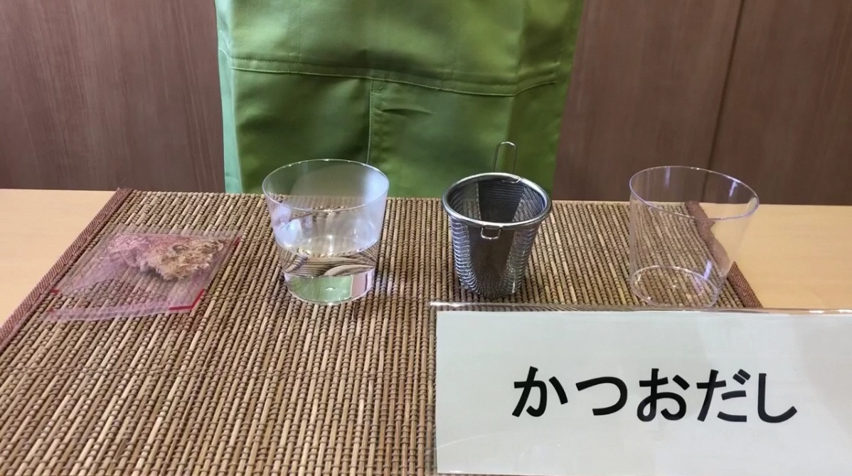 かつおだしと書かれた立て札のそばに液体の入ったコップが並んでいる写真（YouTubeへリンク）