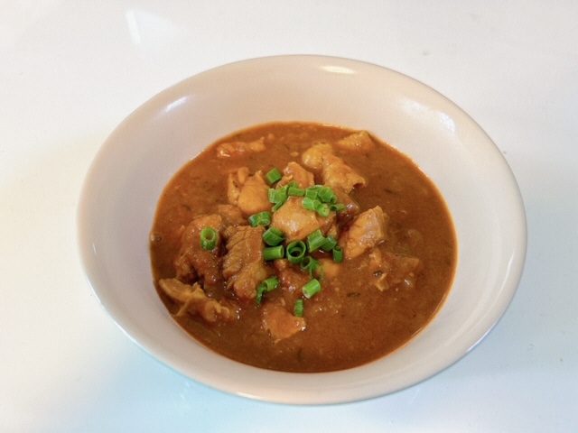 ネギの乗った肉入りカレーが皿に盛られている写真