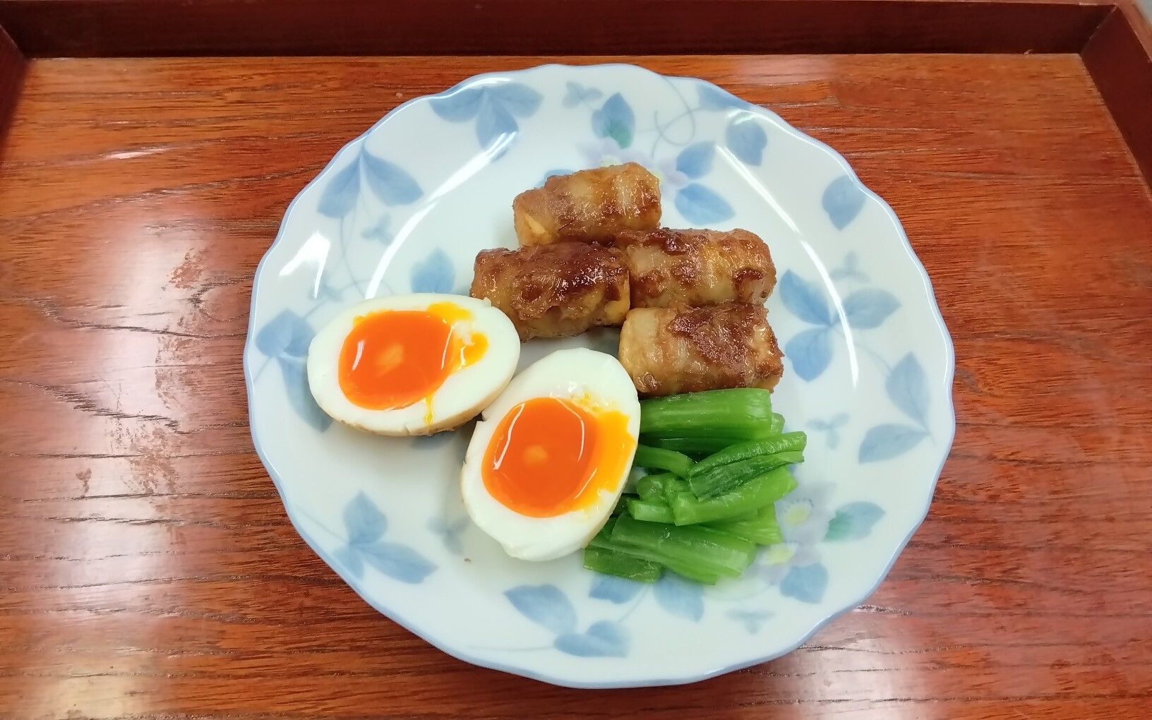 半熟ゆで卵・肉巻き・野菜が盛られた皿の写真