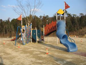 旗のついた滑り台等の遊具がある芝生広場の写真