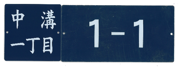 それぞれ中溝一丁目、1－1と書かれた、紺色に白文字で左右の端に穴がある2枚の住居表示板の写真