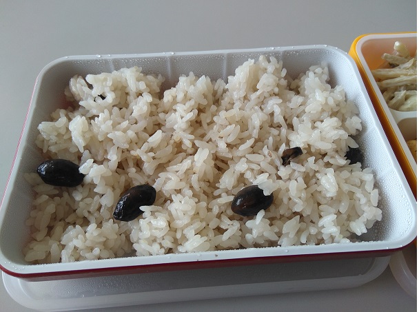 黒大豆がのっていて薄い赤色になっている黒豆ごはんの給食の写真