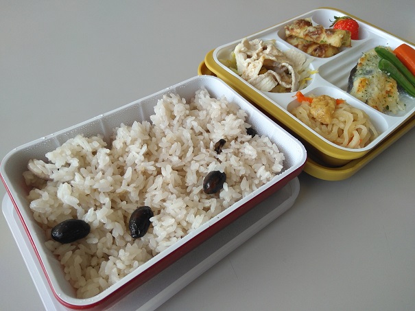 黒豆ごはんとおかずのプレートが並んでいる給食の写真