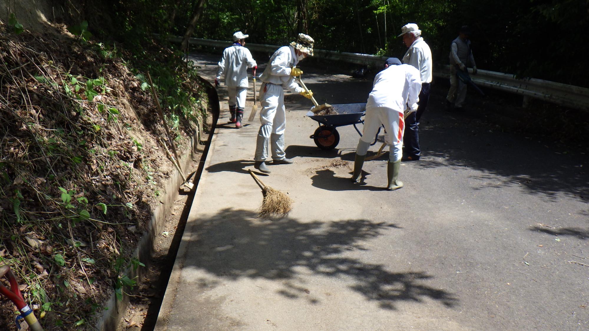 側溝にたまった土砂をスコップで撤去している写真