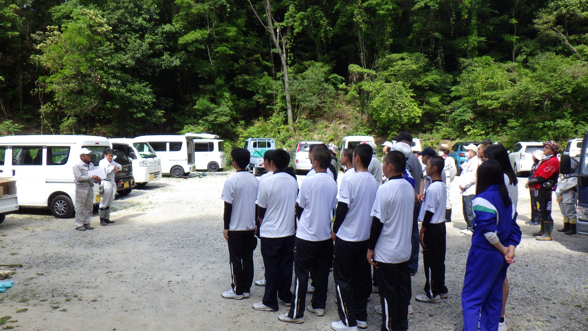 駐車場で縦列になって並んでいる清掃作業の参加者たちの写真