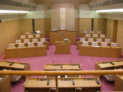 向かい合うように置かれた、たくさんのマイク付きの机と座席の写真