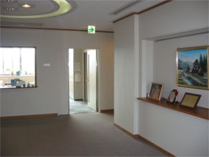 絵画や賞状が飾られた廊下の奥に扉が開いた部屋が見えている写真