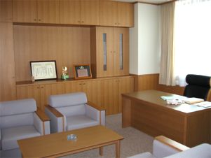 賞状などが飾られた収納棚や応接用の席がある部屋の写真