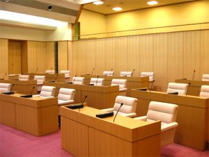 白い椅子の議員席がたくさん並んだ議場の写真