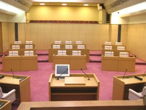 モニターが置かれた演台と奥に並んだ議員席の写真