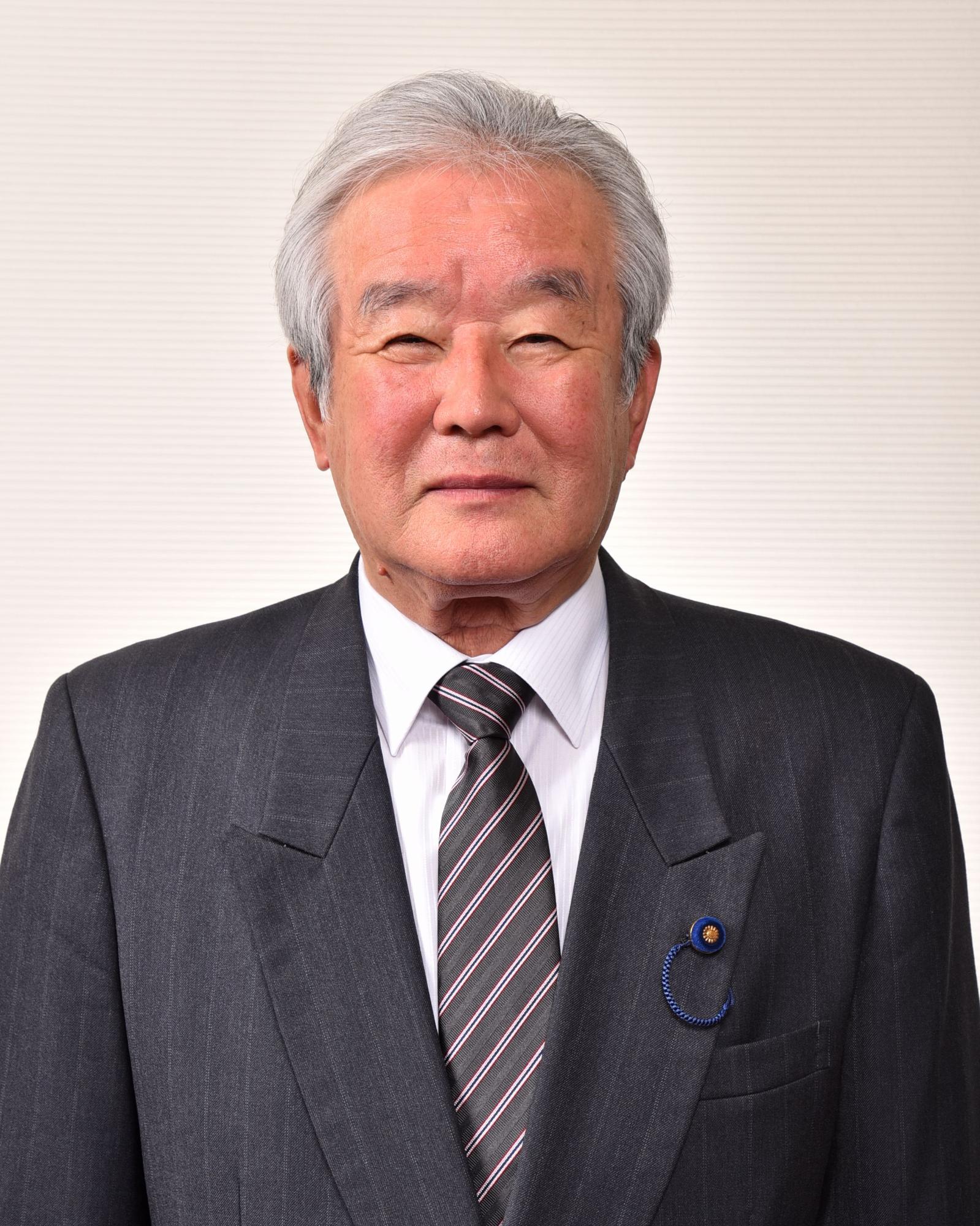 黒のストライプ模様のネクタイを付けている笑顔のスーツ姿の男性の写真