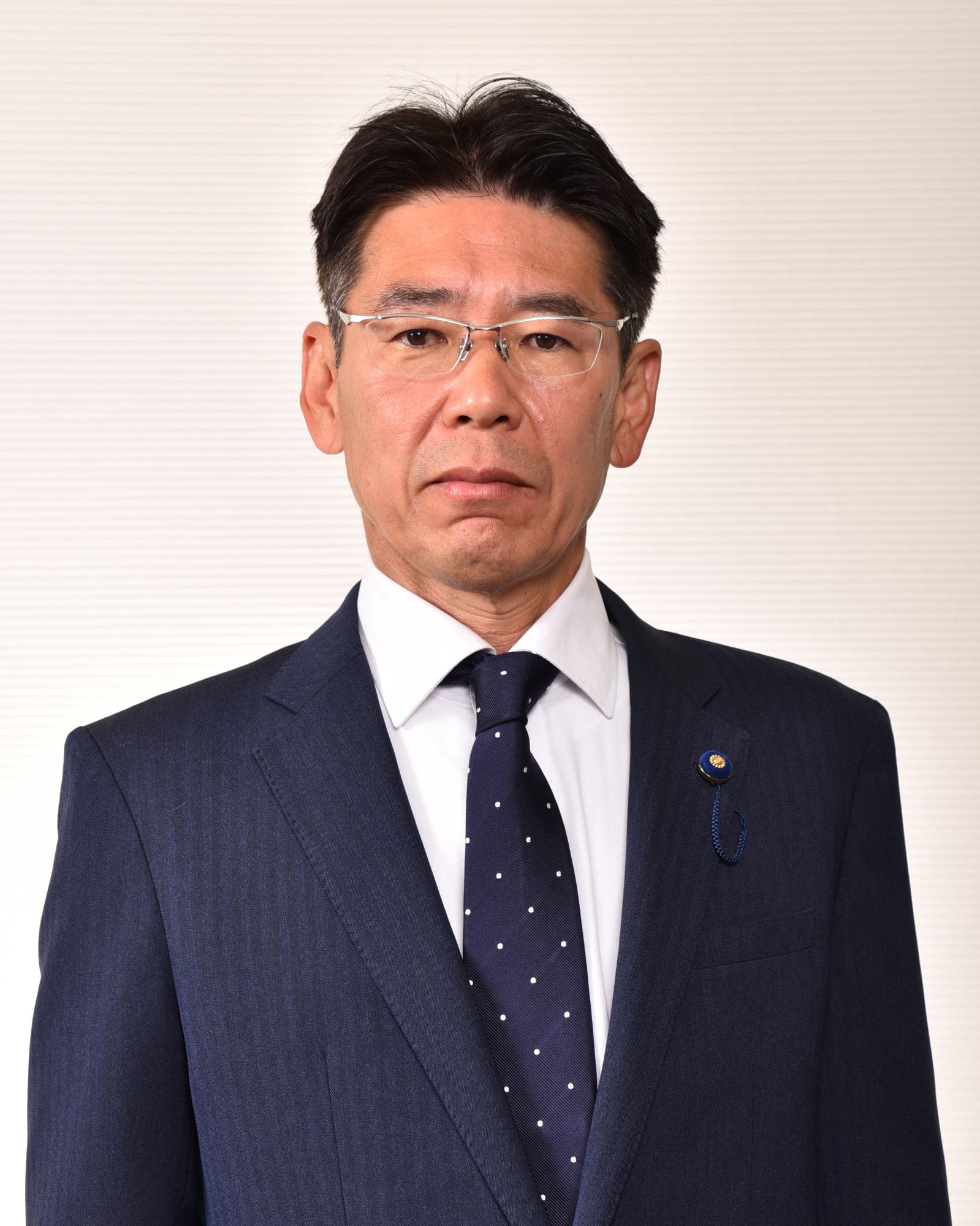 紺のスーツと紺のネクタイを付けている眼鏡をかけた男性の写真