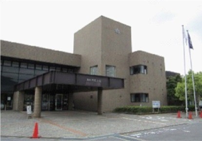 正面玄関の近くに二つの旗が掲げられている灰色の建物の写真