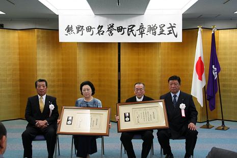 室内で椅子に座った男性と女性が表彰状を周りに見えるように持っている写真