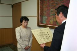 室内で男性が女性に対して賞状を読み上げている写真