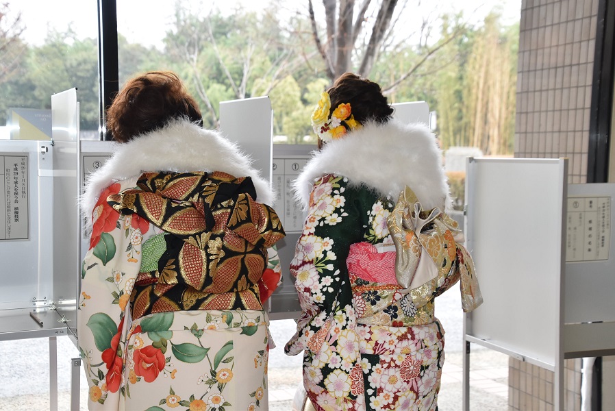 振袖を着た2人が投票所で記入している様子の写真