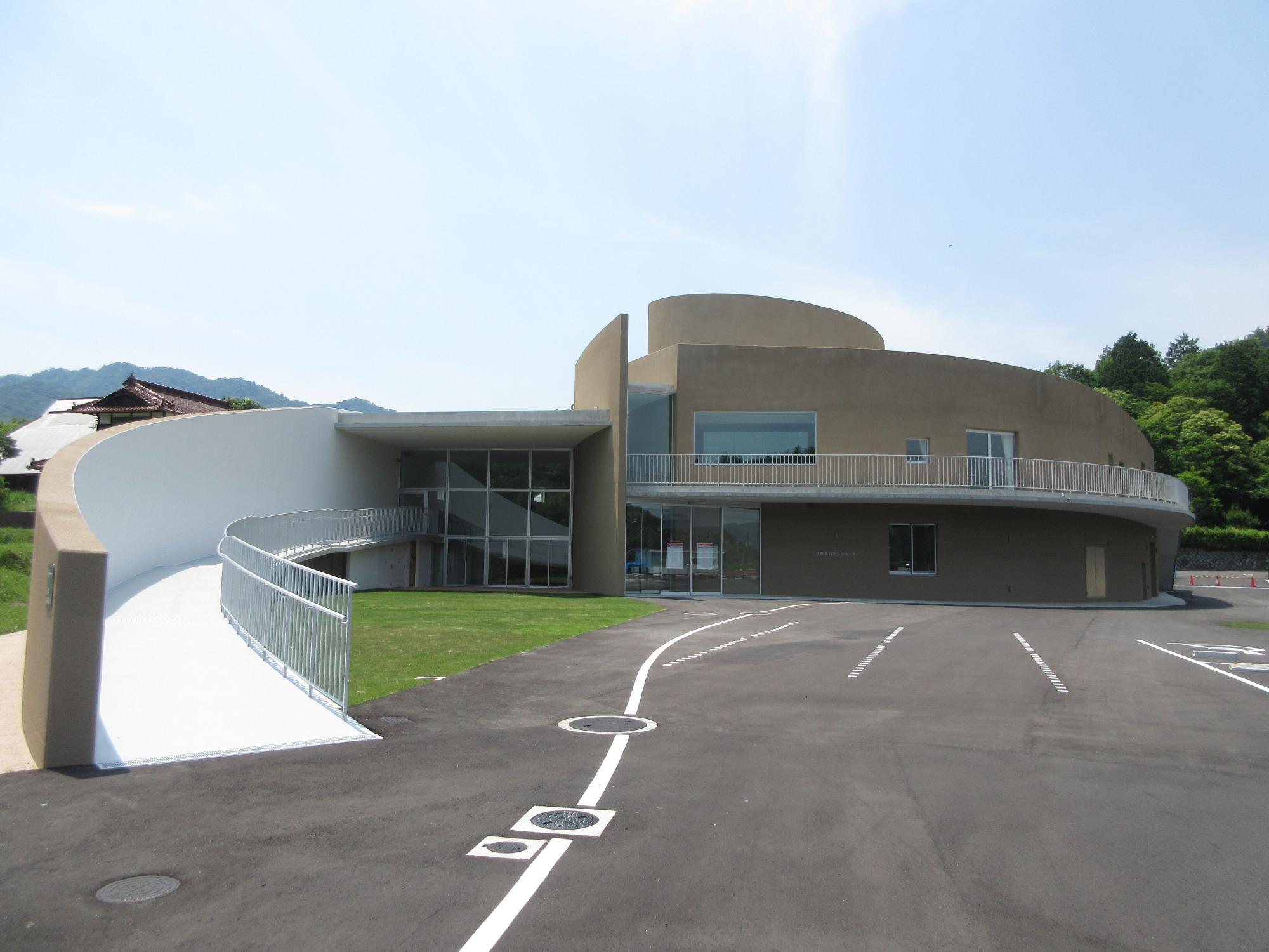 青空の下薄茶色を基調とした建物と遠くに木々が見える写真