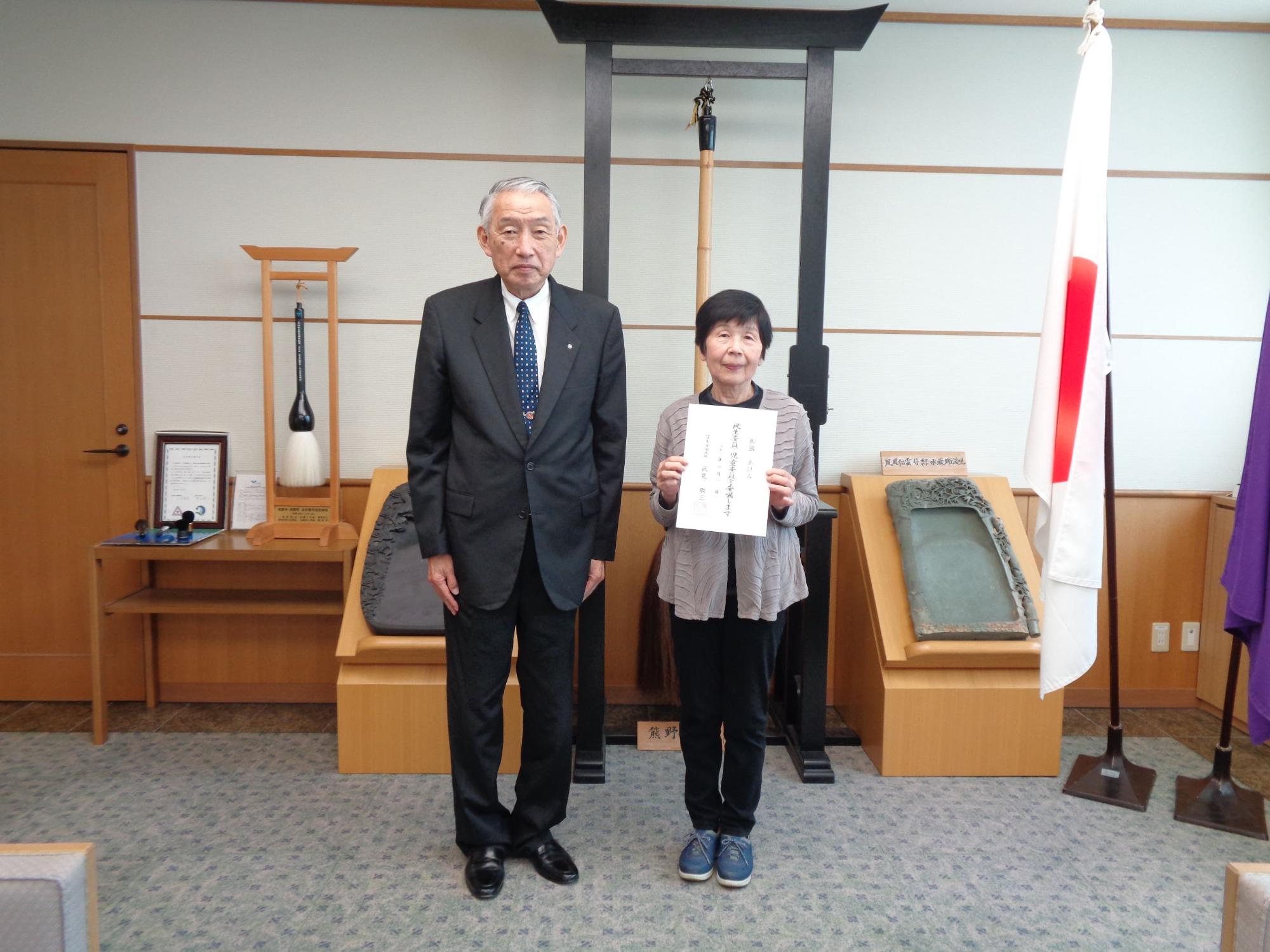 熊野町長の隣に立って委嘱状を手に持つ笑顔の飯國あけみさんの写真
