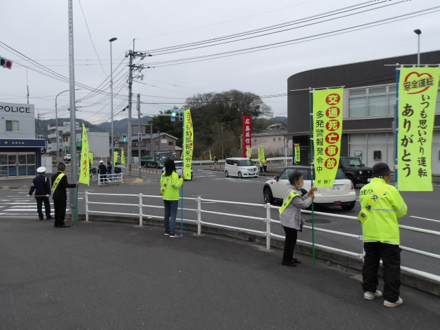 交通安全の黄色いのぼりを持ちながら交差点に立つ地域住民の方々の写真