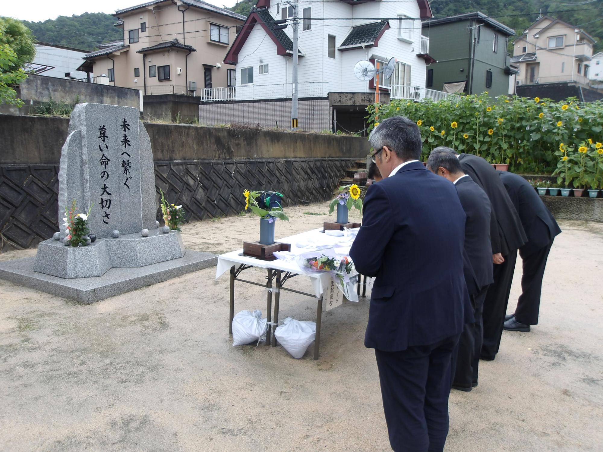 「未来へ繋ぐ尊い命の大切さ」と刻まれた石碑に向かい祈りを捧げる熊野町長ほか町職員の写真