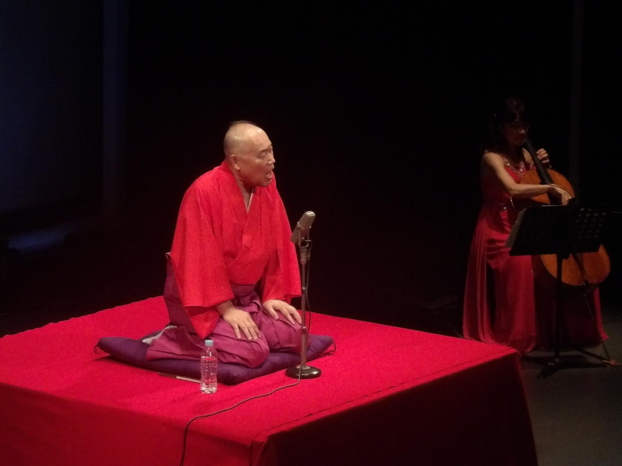 赤い衣装を着て落語を披露する男性の写真