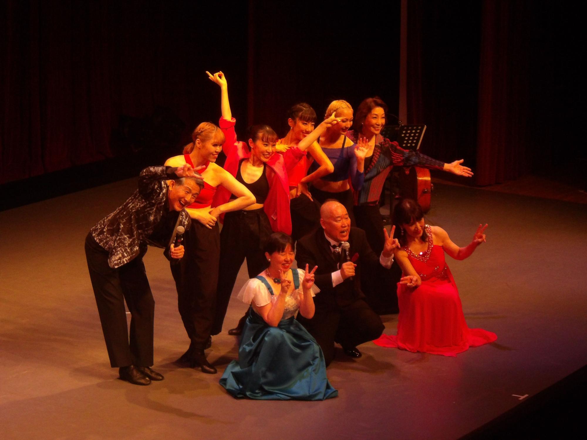 赤や黒などの衣装を身にまとい、ポーズをきめて舞台上での記念撮影に臨むダンサーの方々の写真
