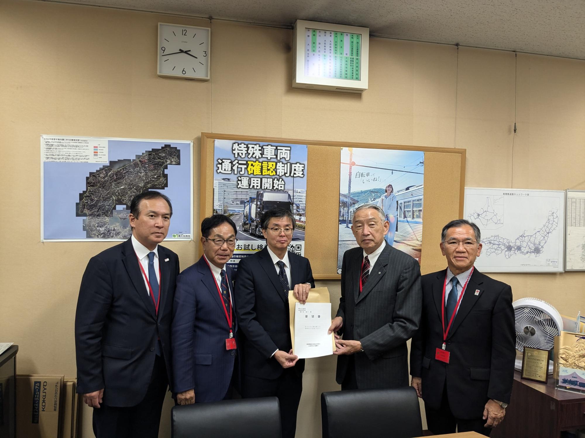 掲示されたポスターの前で記念撮影に臨む国土交通省道路局佐々木次長たちと熊野町長の写真