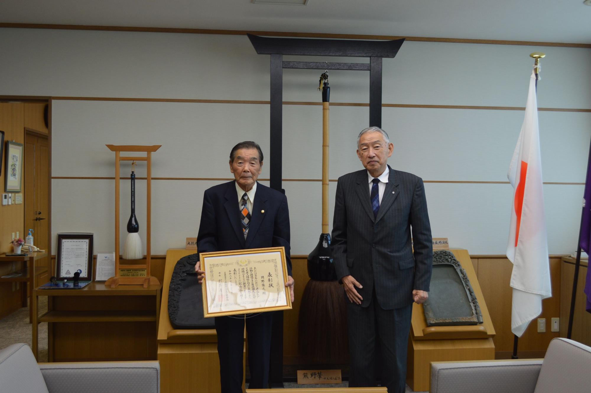 表彰状を手にし熊野町長とともに記念撮影に臨む岡野隆之会長の写真