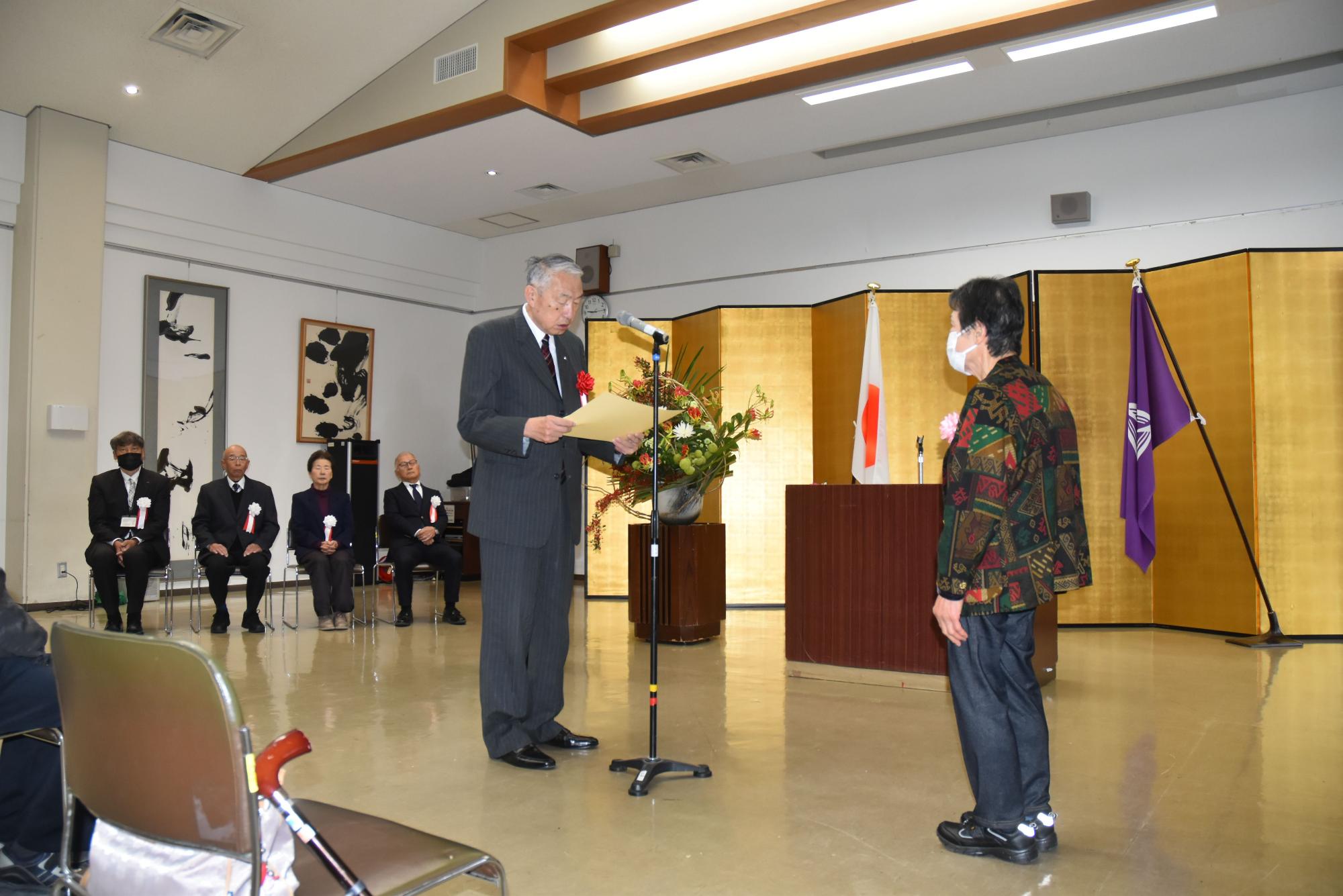 金屏風の会場の表彰式で表彰状を読み上げる熊野町長の写真