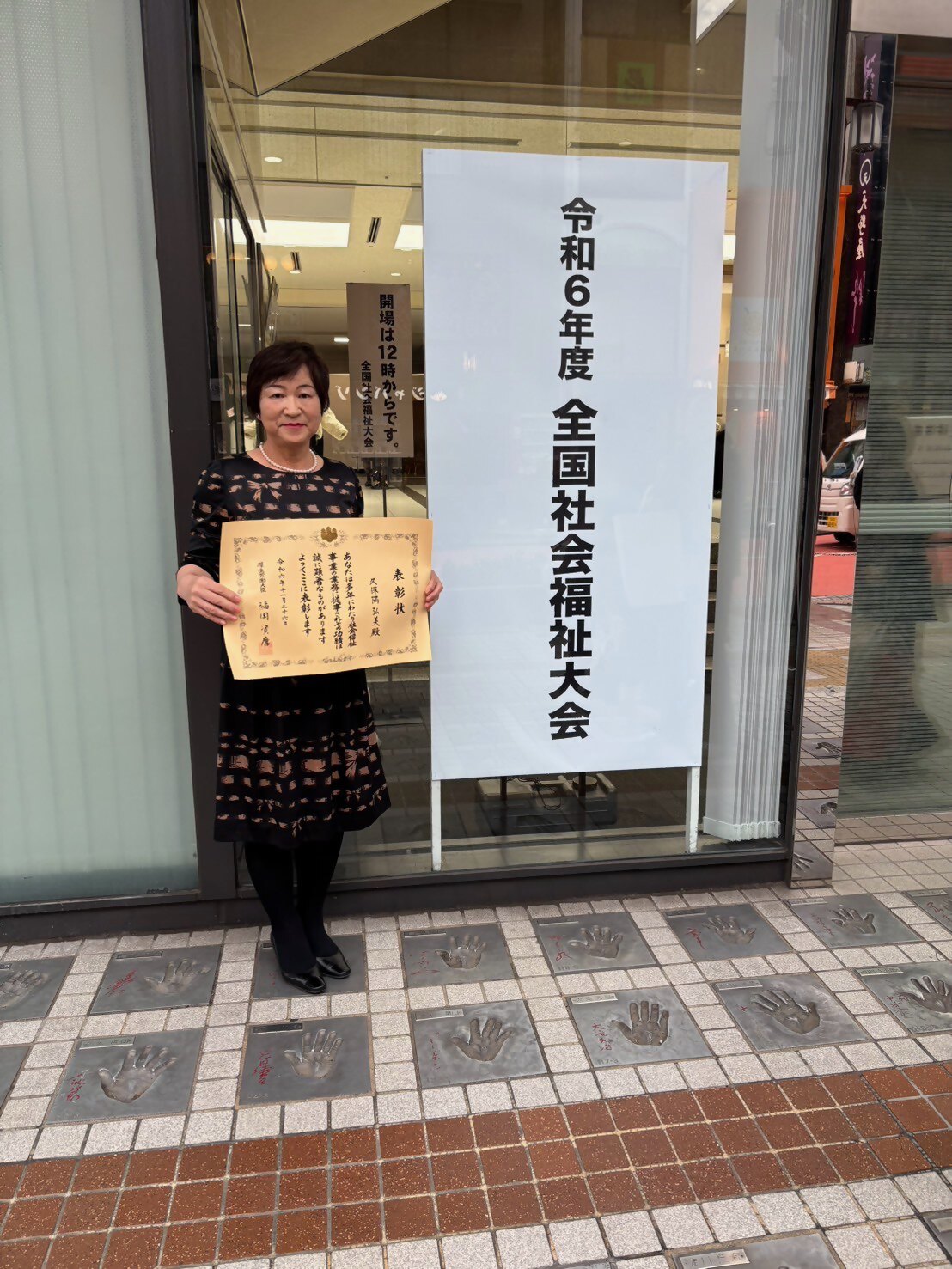 福祉大会の会場入り口で賞状を持ち記念撮影に臨む久保隅弘美さんの写真