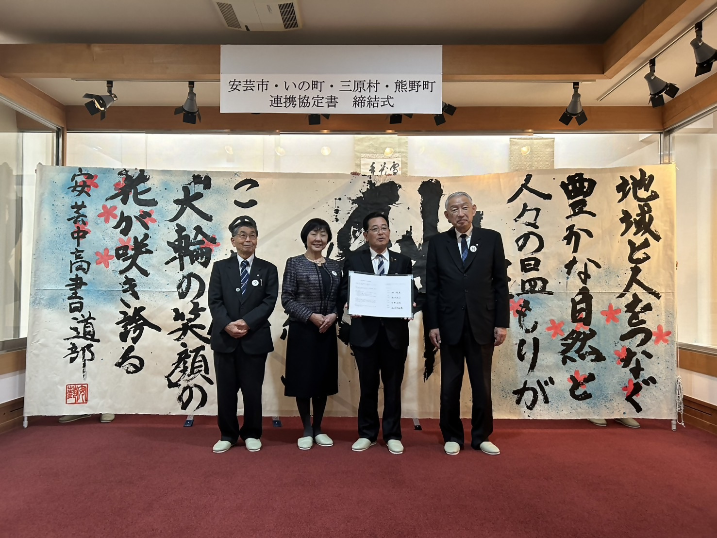 連携協定書締結式で大きな書をバックに記念撮影に臨む熊野町長や他の市町村の代表者たちの写真