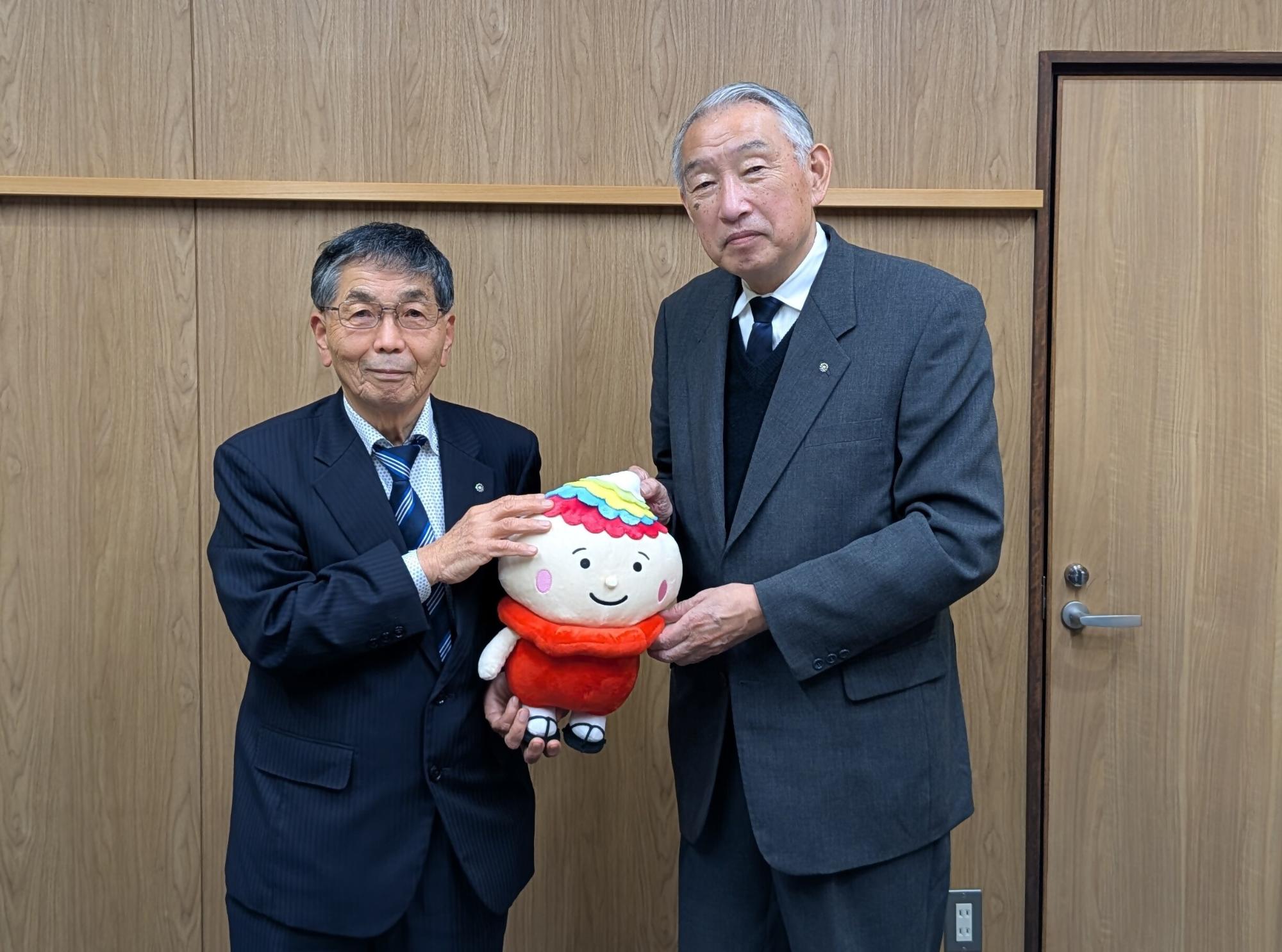 ゆるキャラのぬいぐるみを持ち、記念撮影に臨む三原村の田村村長と熊野町長の写真