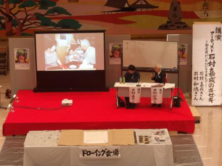 ドローイング会場の壇上で講演を行う石村嘉成さんと父親の和徳さんの写真