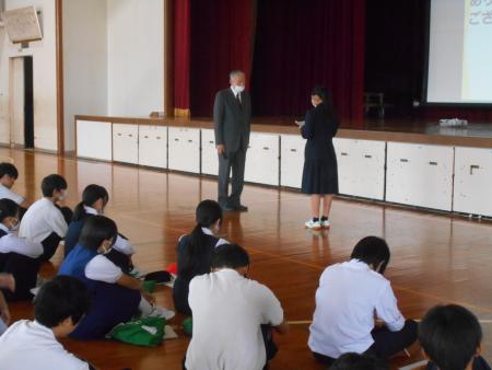 体育館で座っている生徒たちの前で話す生徒と対峙している男性の写真