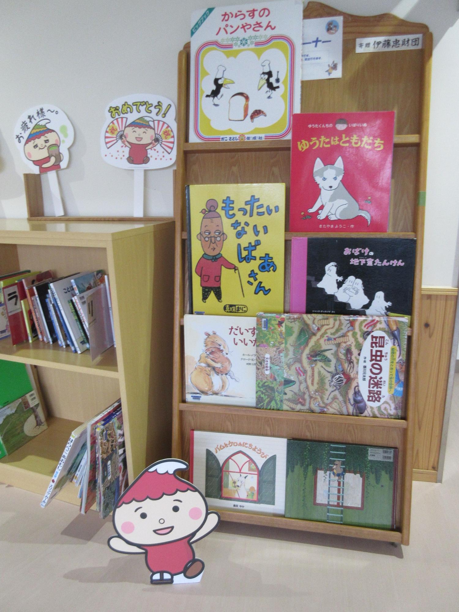 棚に大きな絵本が数冊置かれていて、そばにこふでりんの立て看板がある写真