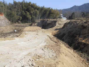 役場庁舎側の道路から土の路面の道が続く先に計画地がある様子を撮影した写真