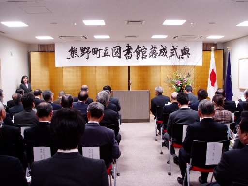 熊野町立図書館落成式典と書かれた横断幕が張られ、出席者が着席している落成式典の写真