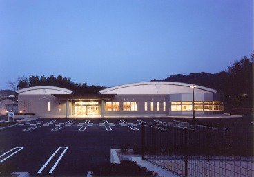 薄暗い空を背景にした、正面入口の扉と窓から明るい光が漏れている図書館の写真