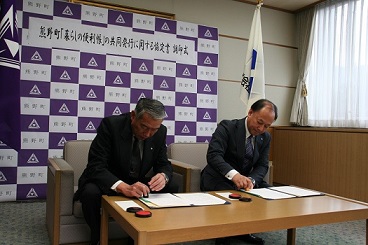 机に並んで座り、それぞれの協定書に調印する株式会社サイネックスの代表者と三村町長の写真