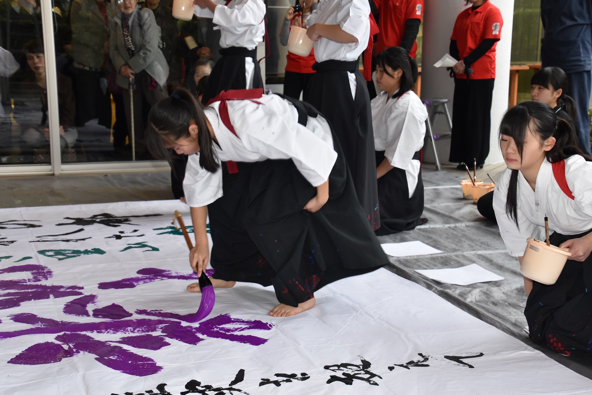 作品の真ん中に紫色で「伝統と誇り」と、力強く思いを込め書き入れる熊野高校書道部員たちの写真