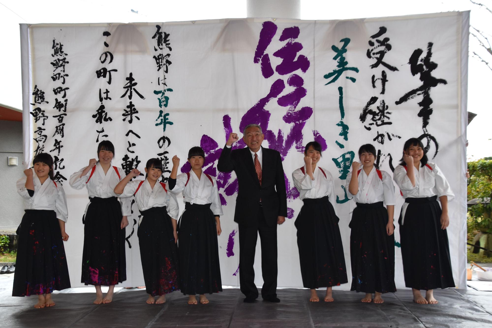 「大書パフォーマンス」で書き上げた作品の前に並んだ袴姿の熊野高校書道部員の生徒たちと三村町長の記念写真
