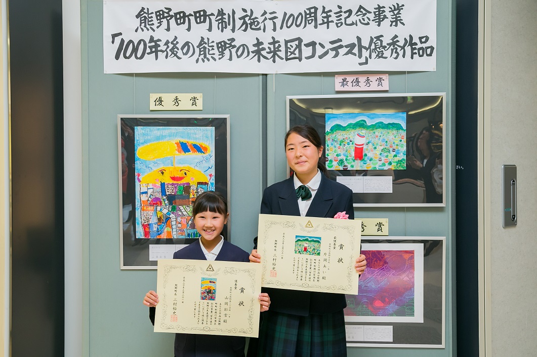 受賞した絵画作品の前に並び笑顔で賞状を掲げている片岡さんと山岡さんの写真