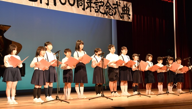 舞台の上に子ども達が並び手に持った歌詞を見ながら「ふるさと」合唱をしている写真