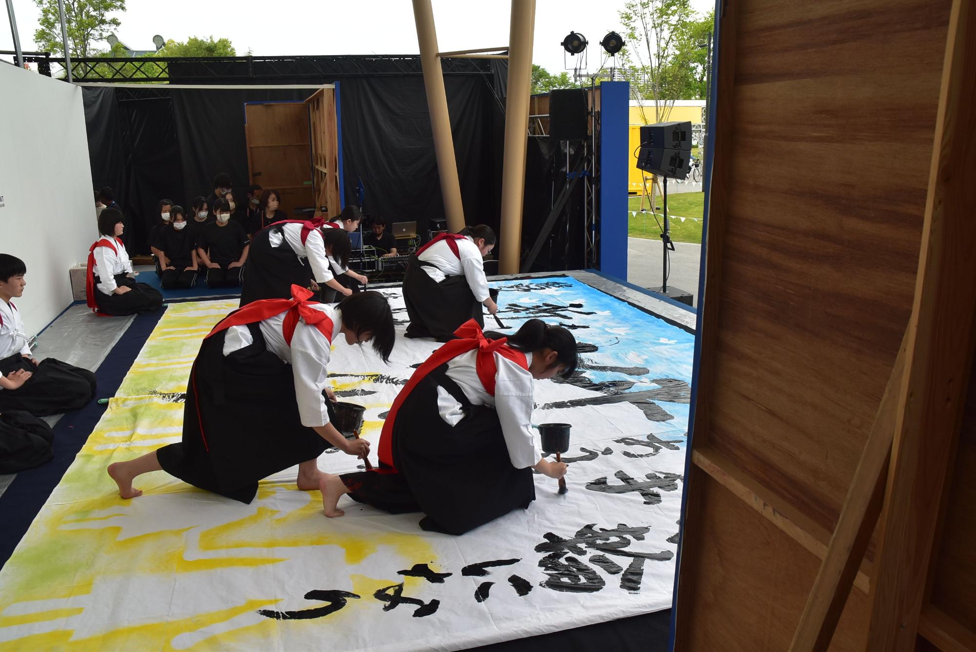 何人もの書道部員が協力して作品を書き上げている様子の写真