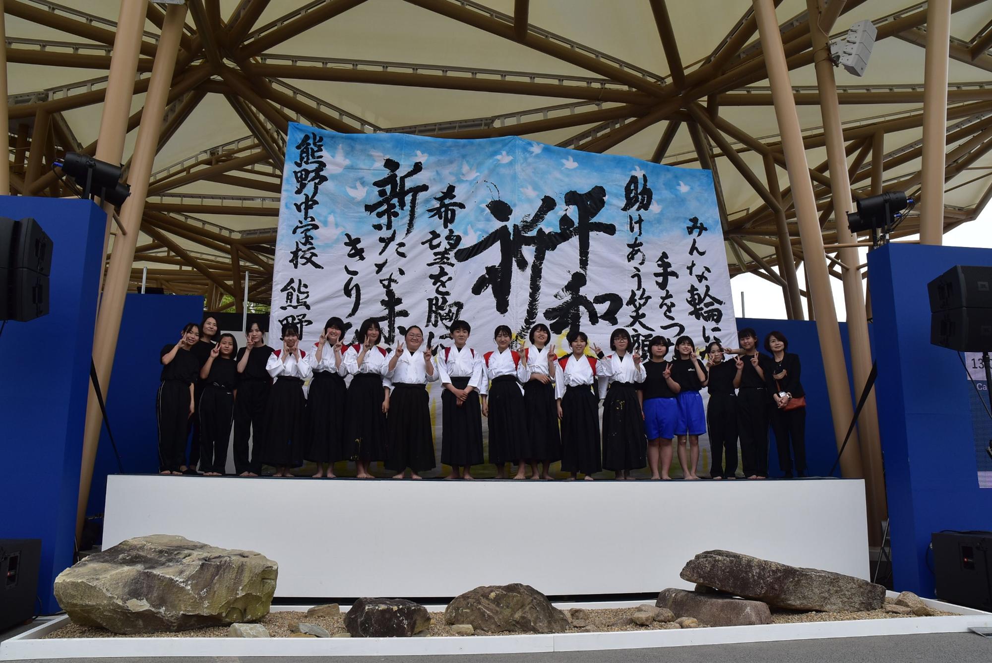 ステージ上に広げられた作品の前に両校の書道部員が整列して撮影された記念写真
