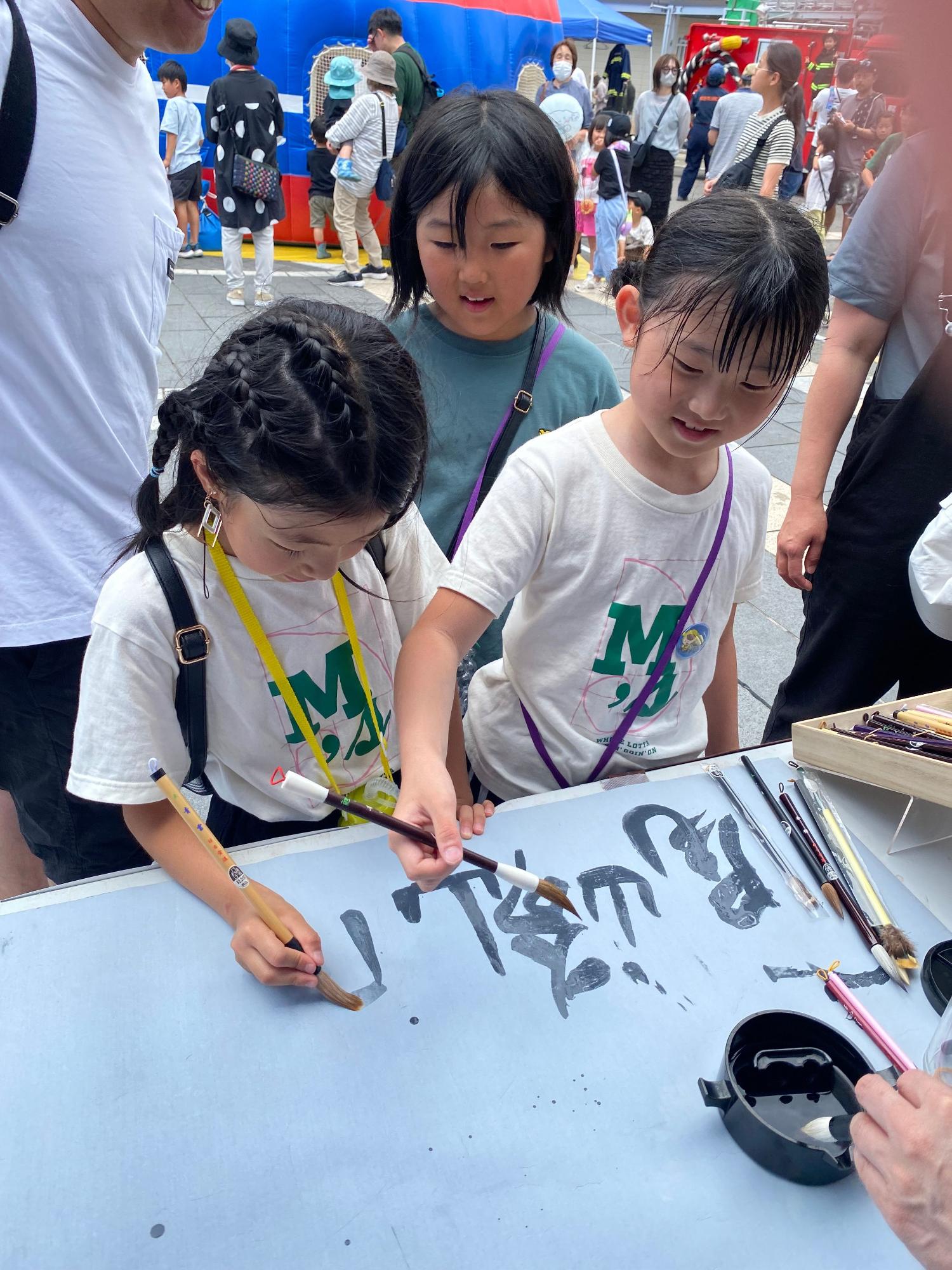 3人の子どもたちが、熊野筆を使って書の体験をしている写真