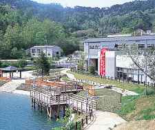 池の上に展望デッキがあり近くに白い建物の施設がある場所を山側から撮影をした写真