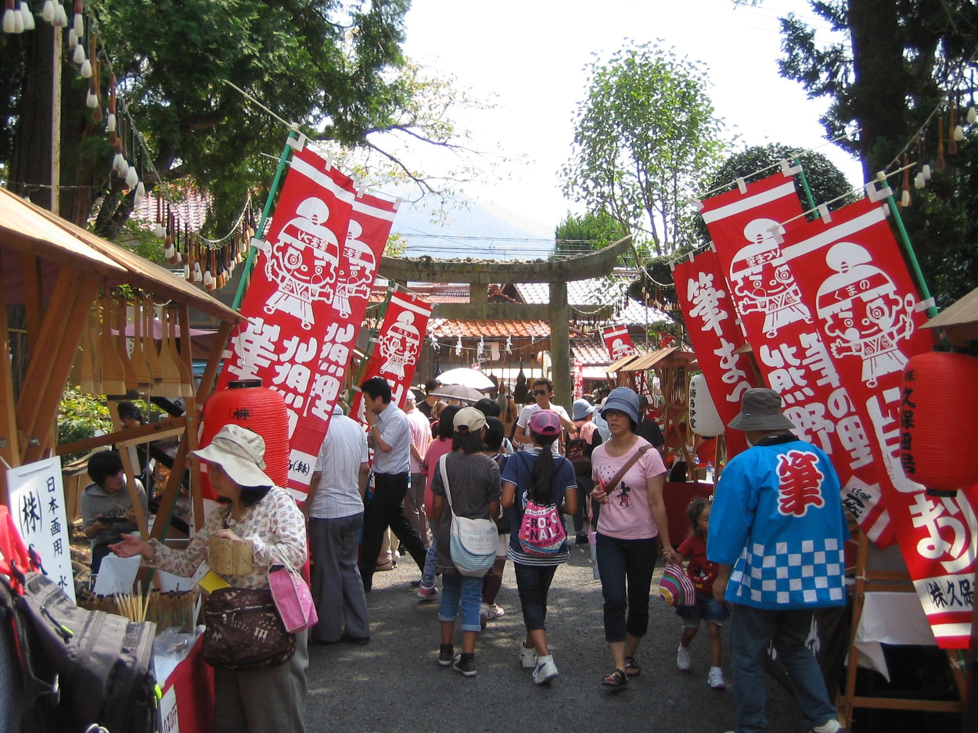 神社の鳥居の前の参道に赤いのぼりや店が立ち並び多くの人が集まる様子を捉えた写真